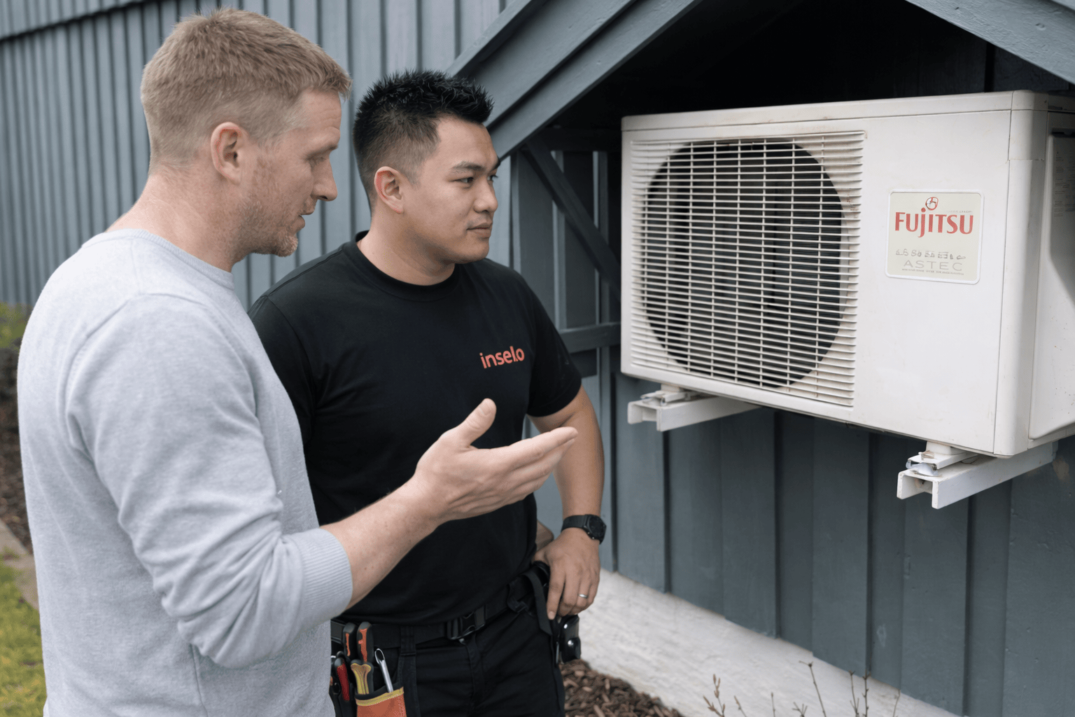 Kunde diskuterer med tekniker om luftvarmepumpen på baksiden av huset